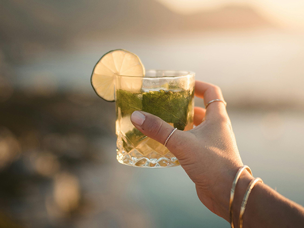 Image of a person holding up a cocktail while looking out at the ocean vista to go with the blog May Event Planning Guide for National Bartender Staffing. pexels-taryn-elliott-6790329